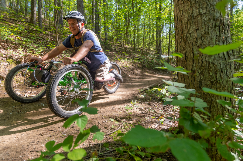 A person on an adaptive bike rides a mountain bike trail in the summer.