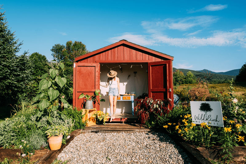 A person inside a red farmstand building seen from outside in summer.