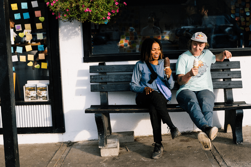 Two people sit on a bench, each holding a cone with soft ice cream.