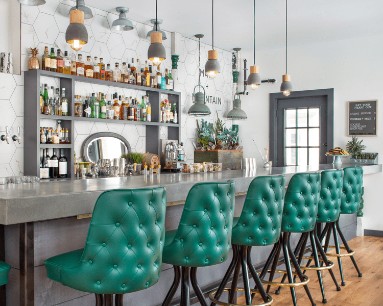 Colorful chairs line an unoccupied bar stocked with alcohol.