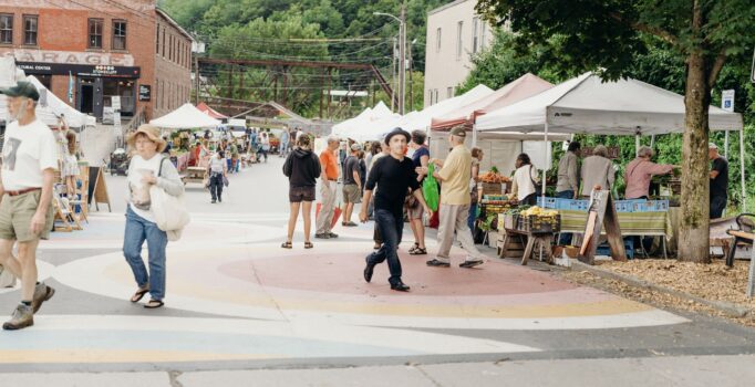 People shop a group of outdoor vendors under tents.