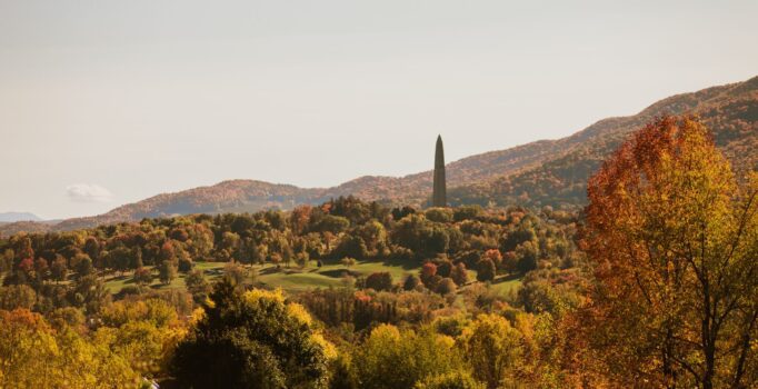 A monument in the distance surrounded by hills with colorful fall foliage in Vermont.