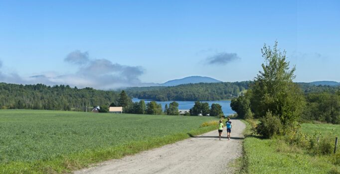 Two people run along a gravel path on a warm and sunny day.