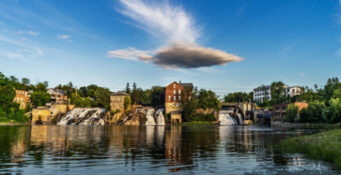Buildings abut a river flowing into a large body of water on a sunny day.