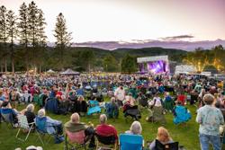 Large crowd sitting in lawn chairs at an outdoor evening concert.