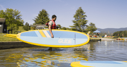 A person carries a paddle board into the water on a sunny day.