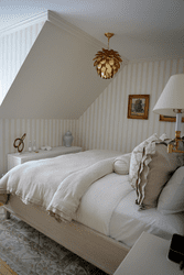 A well-appointed bedroom with lush-looking white linens piled high on a bed with a window.