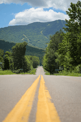 A road stretching ahead with the two yellow lines centered in the image and a mountain ahead.