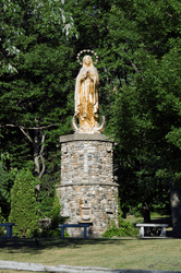 A gold statue of Mary sits on top of a tall rock pedestal base.