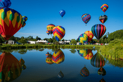 Brightly colored hot air balloons fill a blue sky outdoors in the summer.
