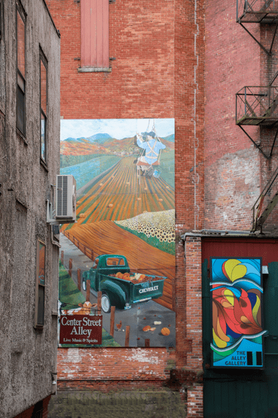 A large painted mural on the side of a brick building. A sign that reads 