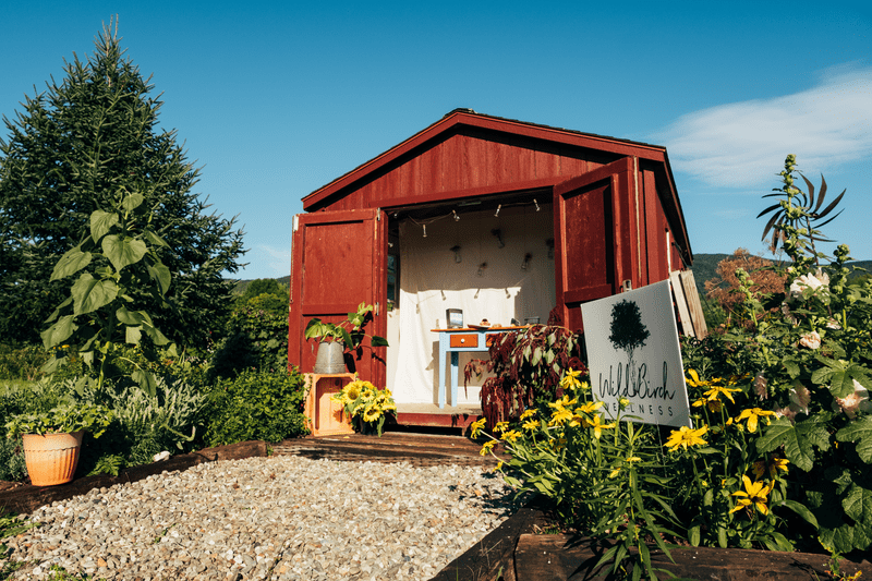 A red building serving as a farmstand seen from outside with flowers blooming.