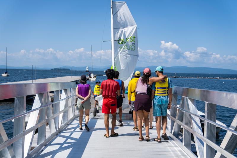 Group of people standing on a dock on the lake preparing to enter a sailboat.