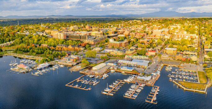 Seen from above, a sprawling rural city lines a large body of water in the setting sun.