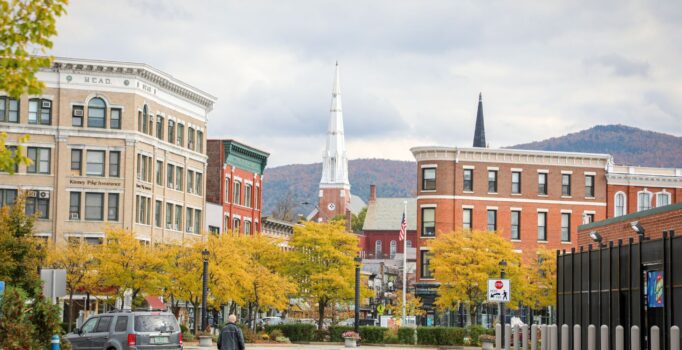 A downtown with historic brick buildings, a white church steeple, and mountains in the background.