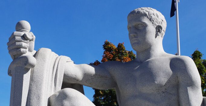 A large granite statue of a man kneeling and holding a sword.