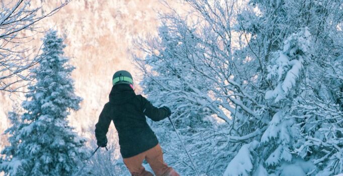 Skier making turns down snowy glades with a sunlit ridge in the background.