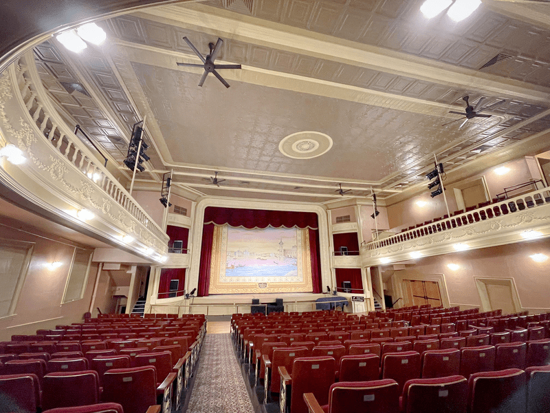 The inside of a historic theatre with red velvet curtains at the stage.