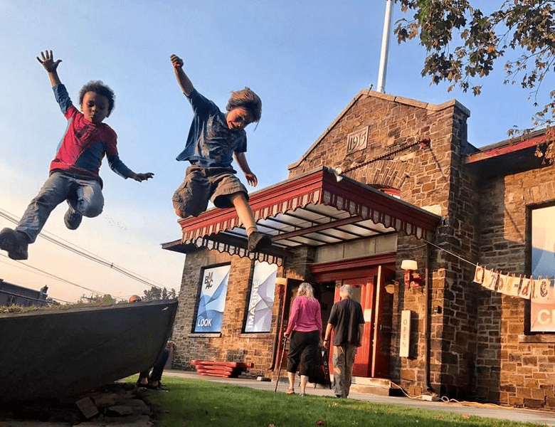 View of 2 kids jumping through the air and a brick building in the background.