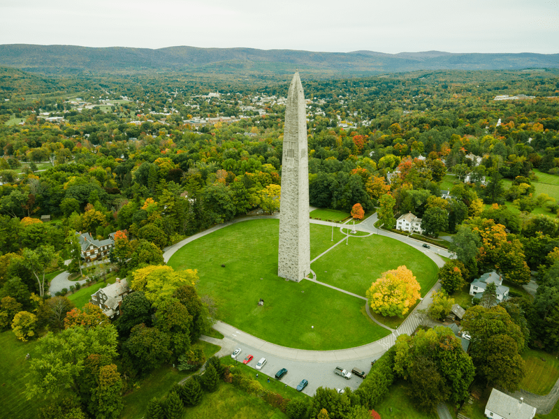 Seen from above, a tall, slender stone monument raises above the trees.