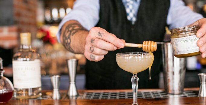 A bartender drizzles honey over a cocktail.