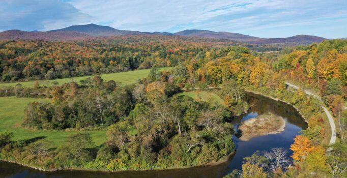 Ariel view of river bend with fall foliage against a blue cloud sky.