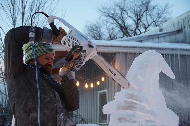 A man uses a chainsaw to carve an ice sculpture.