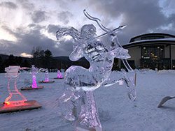Ice sculptures adorn a snowy field outside of a building in winter.