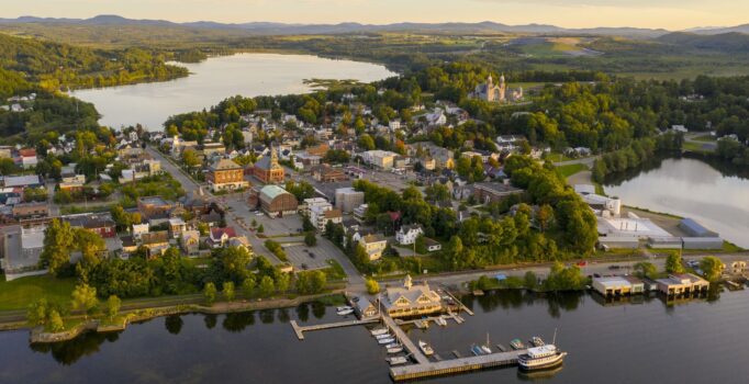Seen from above, a rural town bordering a large bod of water is seen on a summer day.