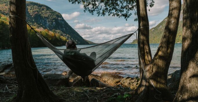 A person lays in a hammock by a large lake.