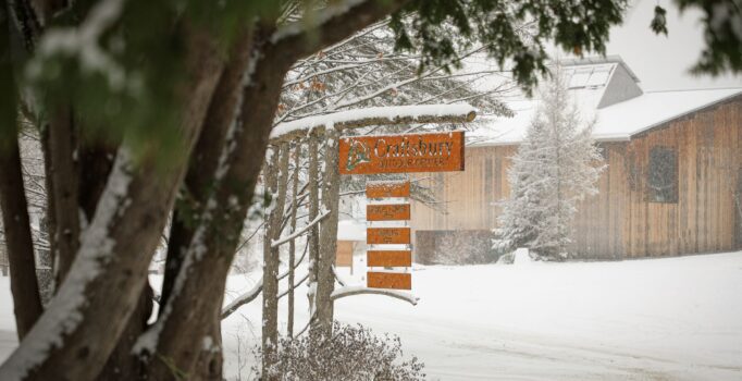 A Craftsbury Outdoor center hangs in front of a wood building on a snowy day.