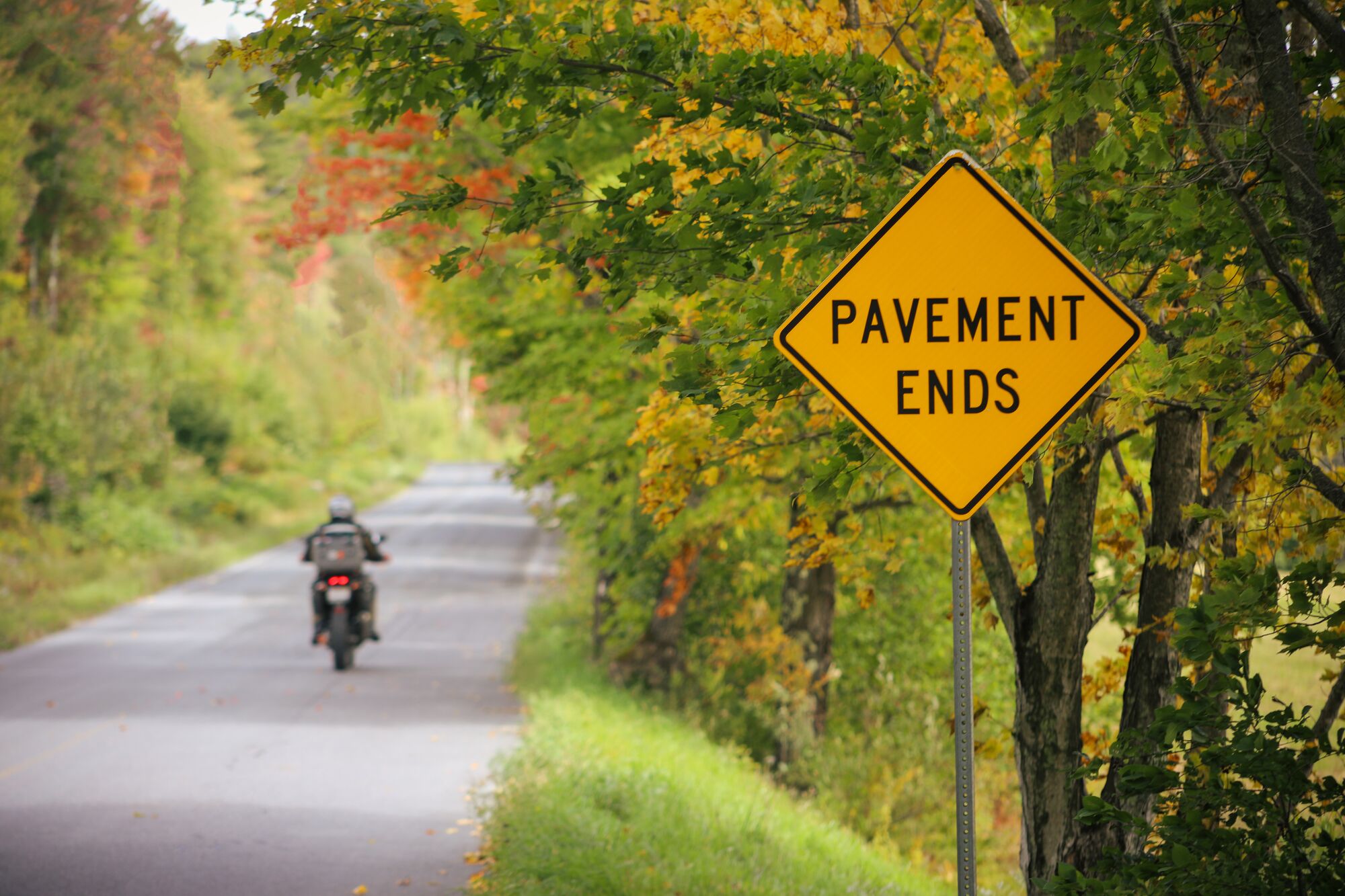 A motorcyclist rides past a road sign that says "Pavement Ends" in Vermont.
