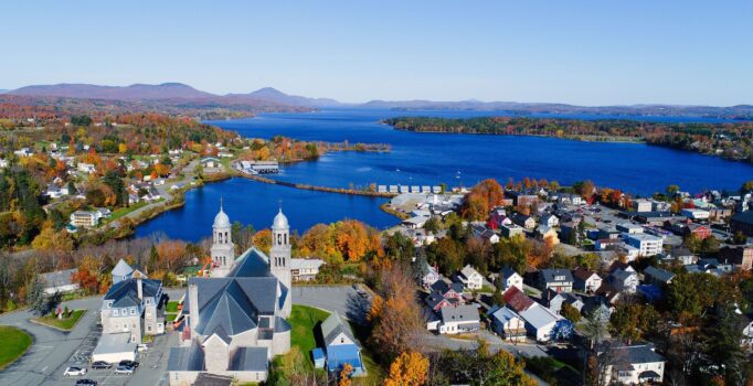 A view from above of downtown Newport that features a stone church in the foreground and a large blue lake in the background.