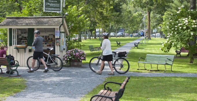 Two people walk bikes on a gravel path through a park.