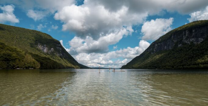 Two paddle boards and a canoe recreate on a large lake surrounded by mountains on a cloudy day.