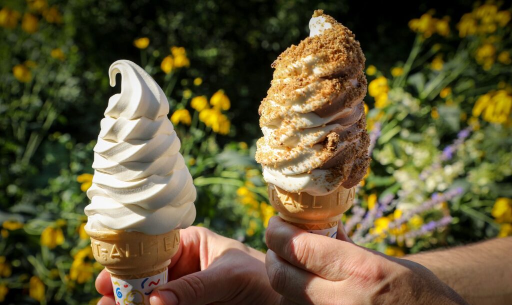 Two ice cream cones full of soft ice cream. One ice cream cone has maple sprinkles.
