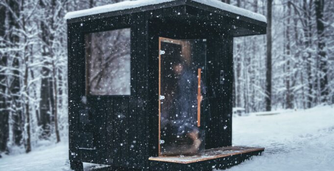 A person walks into a sauna during a snowy afternoon in a forest.