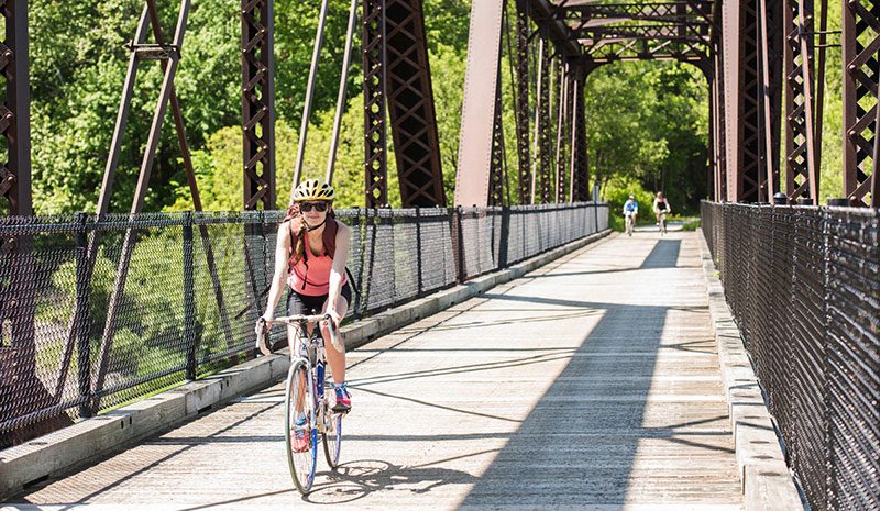 Three people ride bikes toward the camera across a railroad bridge.