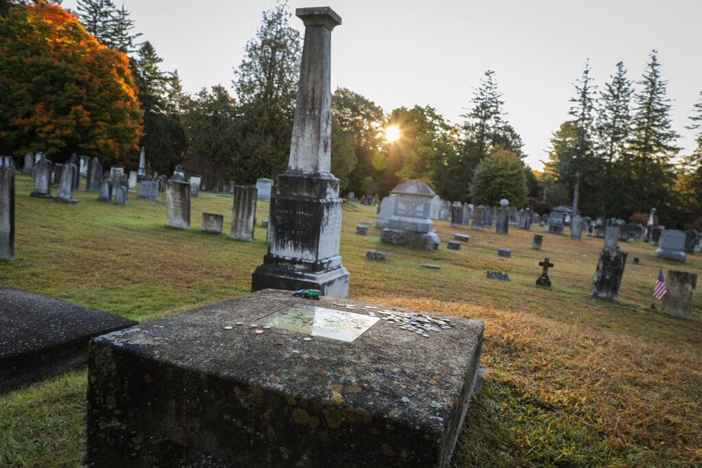 A gravestone with a window surrounded by other graves in a cemetery in the fall.