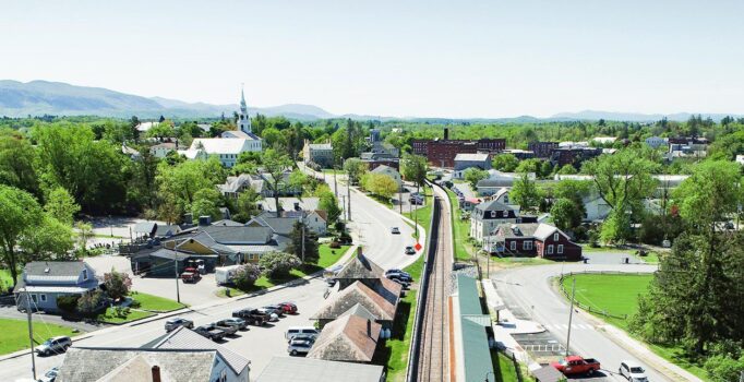 Seen above, a train station is surrounded by green trees on a sunny day.
