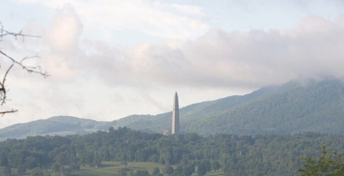Low hanging clouds partially cover a monument that extends above trees in the distance.