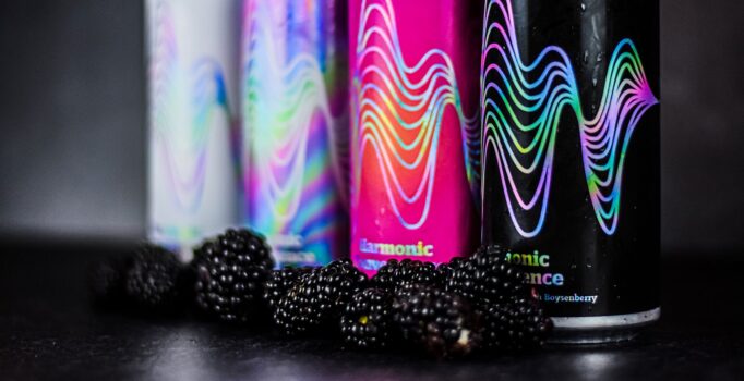 Four craft beer cans and a pile of blackberries are displayed on a black counter.