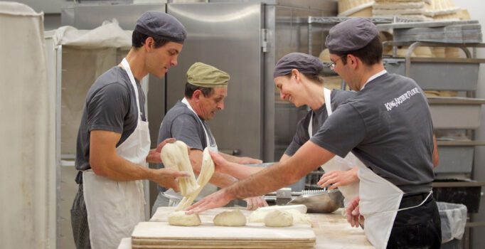 Four people are in a kitchen shaping dough for baking.