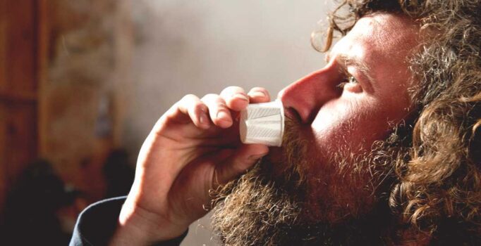A profile-view of a person taking a sip out of a small paper cup.