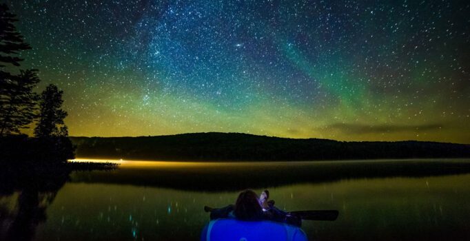 Person floating in a lake at night looking at the night sky full of stars.