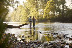 Two people fly fishing in a river in the summer.