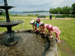 Four children reach their hands into an outdoor fountain in a park.