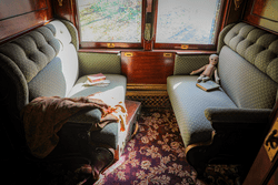 The interior of a historic train car. Two seats face each other with wood paneled walls and floral carpet.