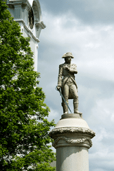 A statue of a soldier is visible against a cloudy sky.