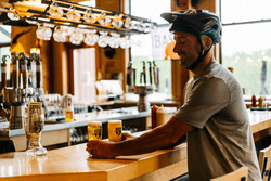 A person wearing a bike helmet picks up to pints of beer from a wooden bar.